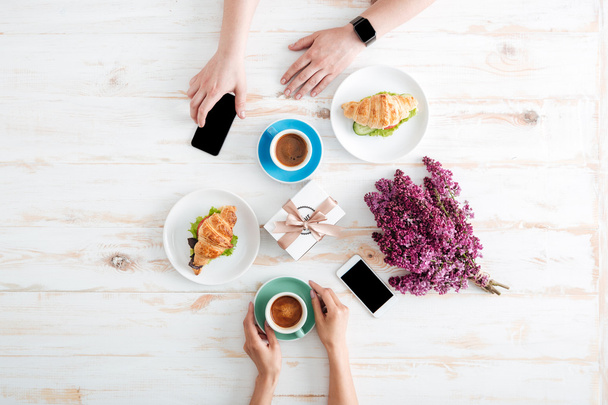 Hands of couple drinking coffee with croissants on wooden table - Valokuva, kuva