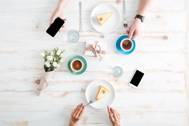 ケーキを食べたり、テーブルの上でスマートフォンを使うカップルの手 - 写真・画像