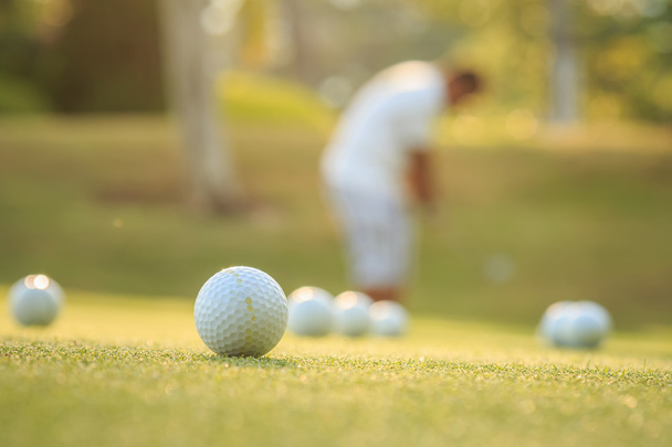 Гольф м'яч і розмитий чоловік грає в гольф в зеленому полі
 - Фото, зображення