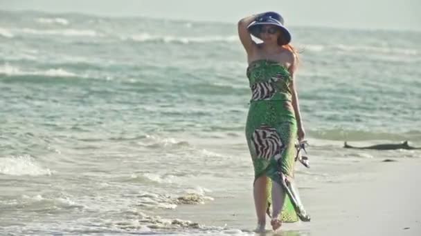 Jonge vrouw In lange jurk en hoed wandelen langs de zee, slow-motion - Video