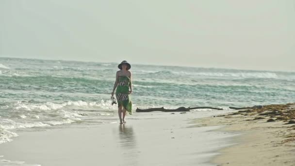 Jonge vrouw In lange jurk houdt schoenen en wandelen langs de zee, slow-motion - Video