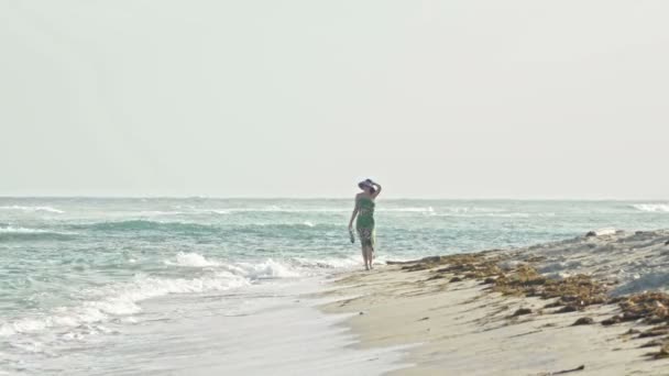 junge Frau im langen Kleid behält die Schuhe und geht am Meer entlang - Filmmaterial, Video