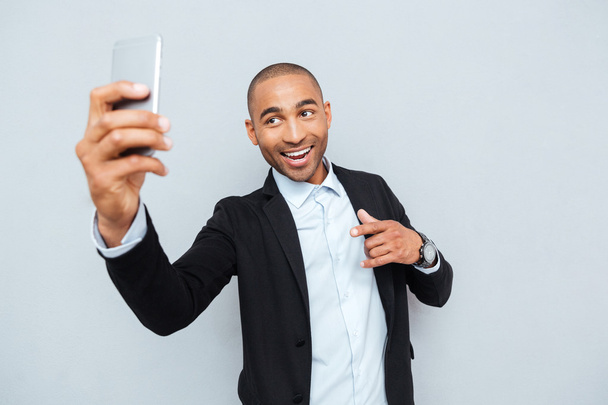 Young man making selfie photo on smartphone over gray background - Фото, зображення
