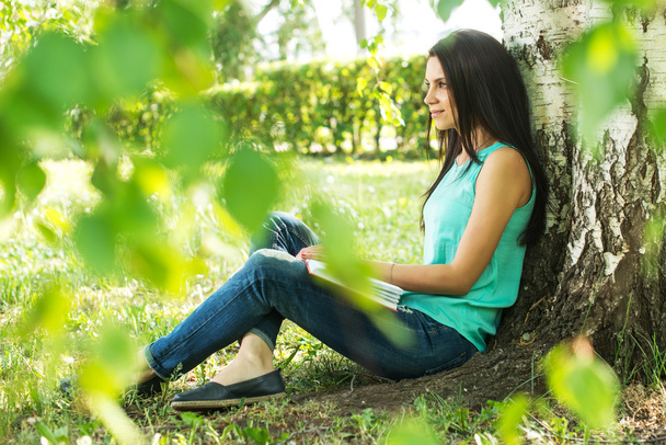 Beautiful woman relaxing outdoors on grass about tree - Fotoğraf, Görsel