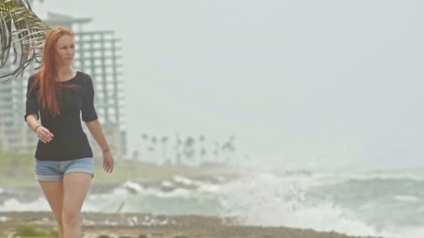 Молода приваблива жінка з довгим рудим волоссям, що йде уздовж штормового моря, повільний рух
 - Кадри, відео