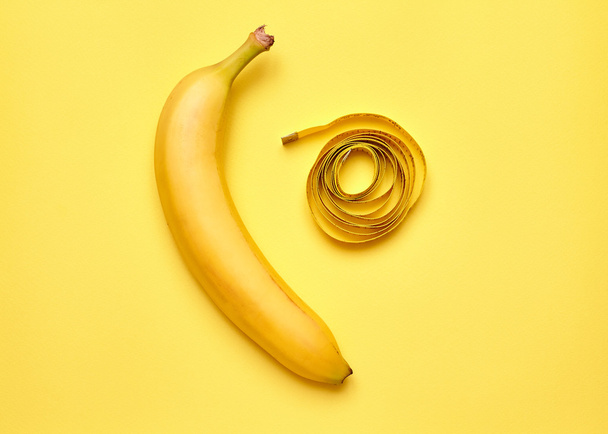 Isolated banana with measuring tape on a yellow background - Φωτογραφία, εικόνα