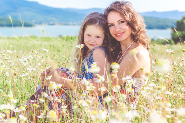 Mother and daughter are sitting in chamomile field - Fotoğraf, Görsel
