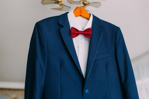 Close-up of excellent expensive blue suit with red bow-tie hanging on luster - Fotografie, Obrázek