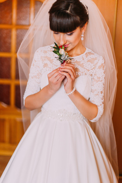 Beautiful bride smells cute floral boutonniere in dressing room before wedding - Foto, Imagen