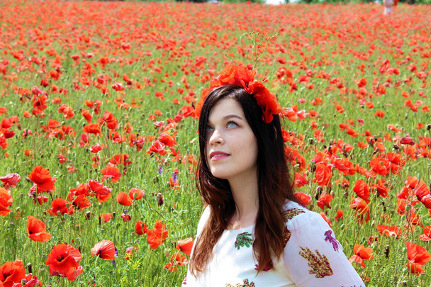 Young woman sitiing in poppies looking up - Photo, Image