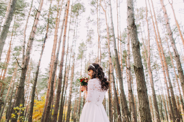 Beautiful innocent young brunette bride in gorgeous white dress with bouquet at pine wood forest - Valokuva, kuva