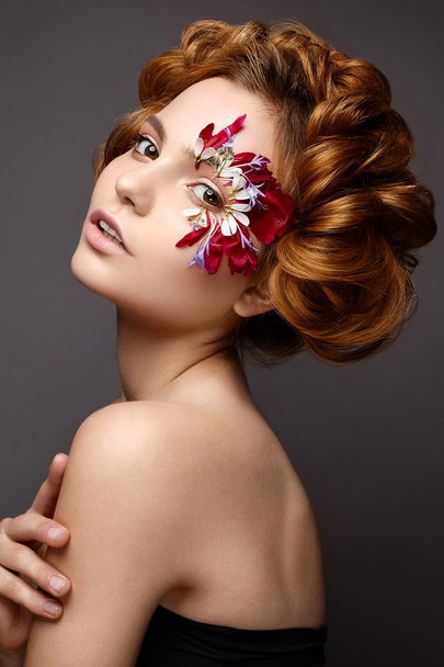 Beautiful girl with creative make-up with floral appliques. The model in the style of romantic with flower petals around her eyes. - 写真・画像