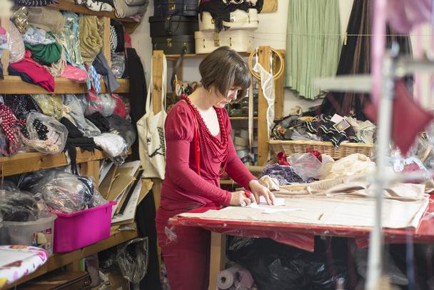 Dressmaker in Red Working on Cutting Table - 写真・画像