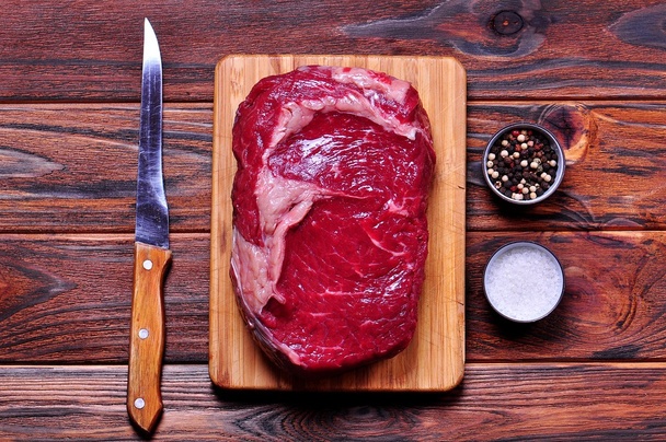 Raw beef rib eye steak on a bamboo chopping board on wooden background. - Фото, изображение