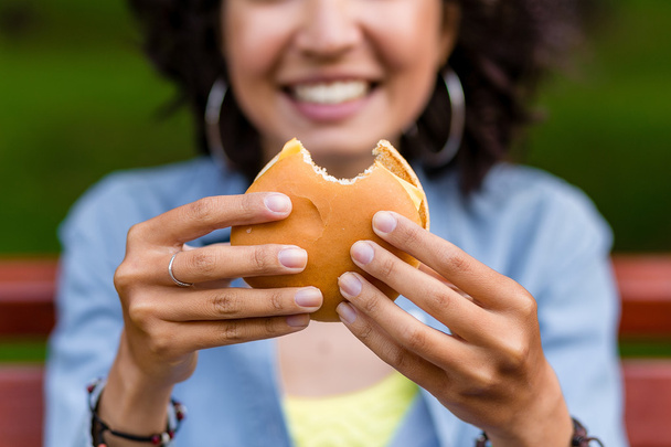 屋外ファーストフードのハンバーガーを食べる若い女性。焦点を当てる、  - 写真・画像
