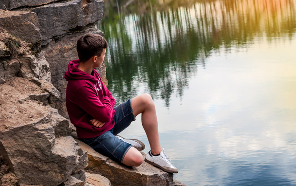 Adolescente vicino al lago si siede su una roccia
 - Foto, immagini
