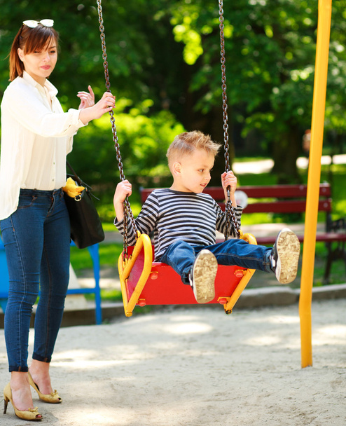 Mother with child playing on swing playground in summer  park - 写真・画像