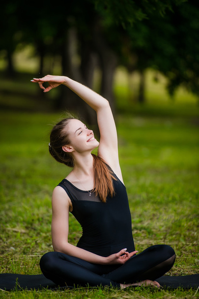 Piękna młoda kobieta robi ćwiczenia rozciągające na zielonej trawie w parku. Trening jogi - Zdjęcie, obraz