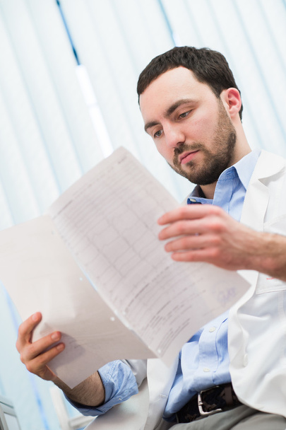 Male medicine doctor checking something at his papers. Medical care, insurance, prescription, paper work or career concept. Physician ready to examine patient and help. - Photo, Image