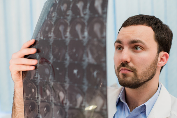 Retrato de primer plano del personal de salud del hombre intelectual con bata blanca, mirando la imagen radiográfica de rayos X del cerebro, escáner ct, resonancia magnética, antecedentes de la clínica. Departamento de Radiología
 - Foto, imagen