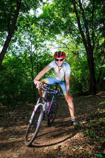 Молодой человек стоит и улыбается в лесу на велосипеде
 - Фото, изображение