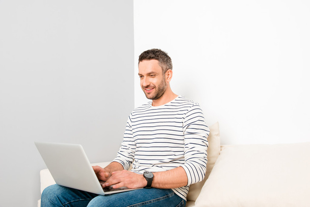 Portrait of happy handsome man sitting on couch and typing on la - Фото, зображення