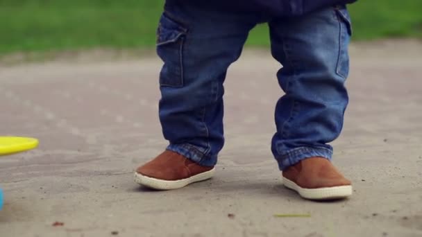 Lindo niño pequeño en pantalones vaqueros azules caminando cerca de monopatín. Patas de bebé
 - Metraje, vídeo