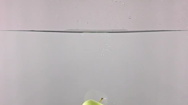 Green apple falling down in water against gray background, super slow motion - Video