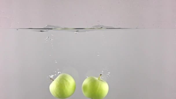 Two green apples fall down in water against gray background, super slow motion - Video