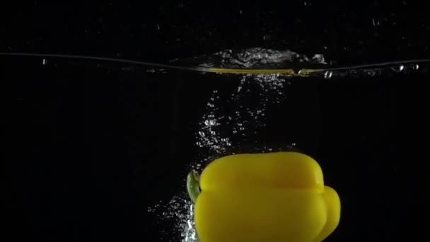 Sweet yellow pepper falls down in water, black background super slow motion shot - Filmati, video