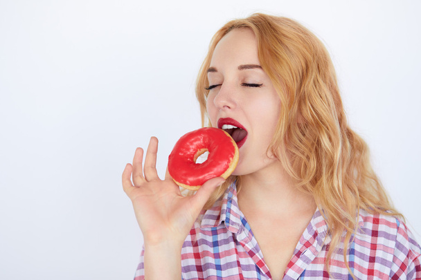blonde woman biting a red donut - Foto, afbeelding