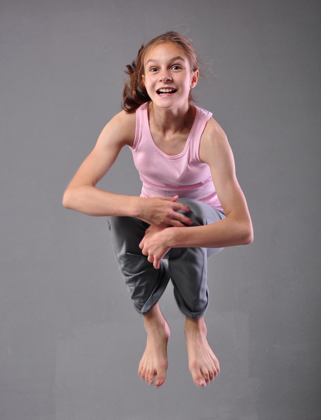 Zdravá mladá šťastná dívka s úsměvem přeskakuje a tančí ve studiu. Dětský cvik skákání na šedé pozadí. - Fotografie, Obrázek