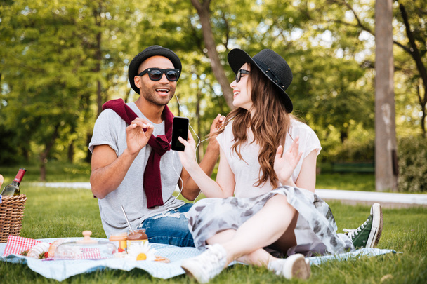 Smiling couple listening to music from cell phone on picnic - 写真・画像