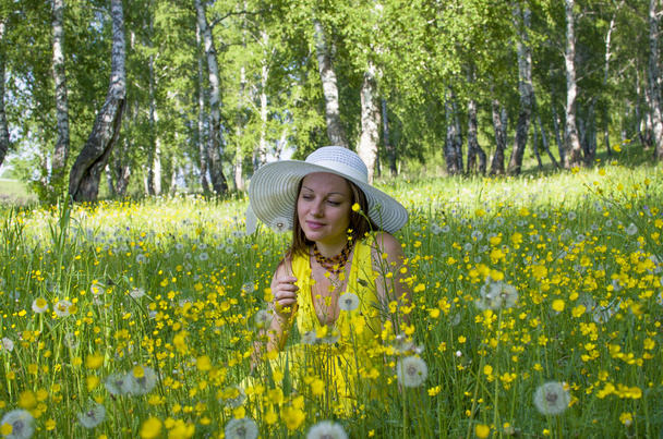 The girl in a hat on a meadow among yellow flowers and dandelions - Fotografie, Obrázek