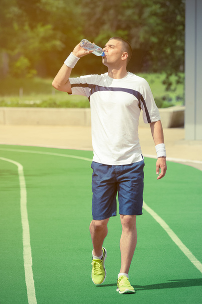 Jogger walking on the running track and drinking water from the bottle - Фото, изображение