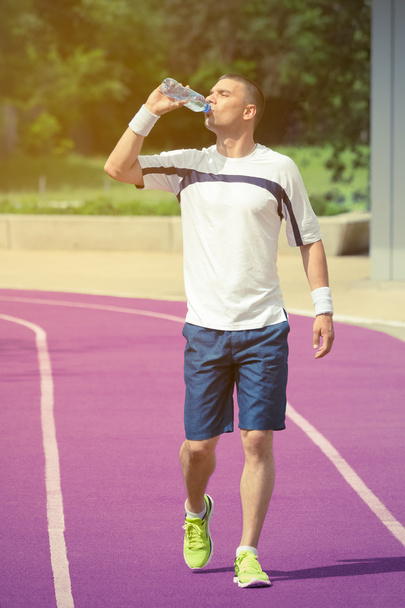 Jogger walking on the running track and drinking water from the bottle - Fotografie, Obrázek