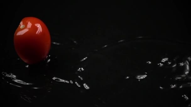Cut red tomato falling down on black watered surfaces. Super slow motion shot - Felvétel, videó
