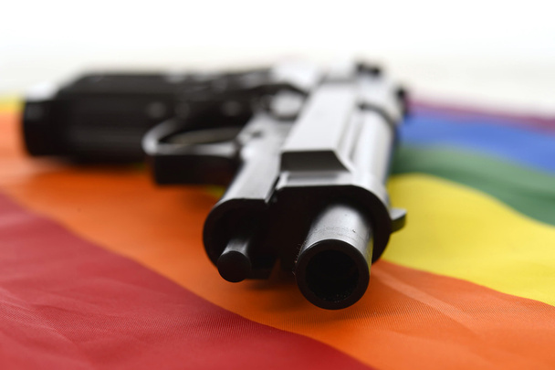 Stillleben mit Nahaufnahme-Waffe, die auf der Flagge der Schwulenparade ruht, die sexuelle Diskriminierung und Intoleranz symbolisiert - Foto, Bild