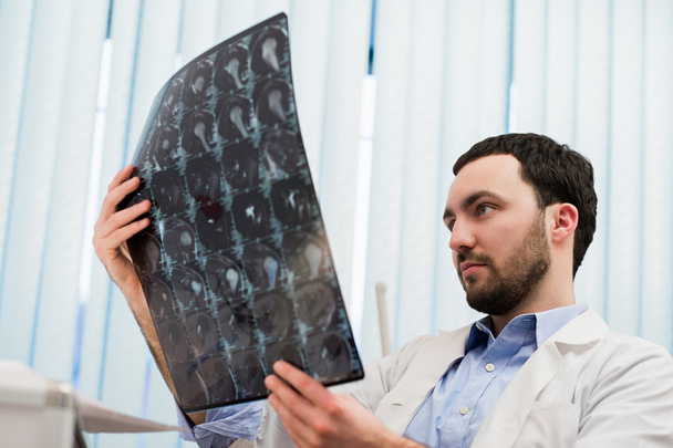 Lähikuva muotokuva henkisen miehen terveydenhuollon henkilöstön valkoinen labratakki, tarkastellaan aivojen röntgenkuva, röntgenkuva, magneettikuvaus, klinikan toimiston tausta. Radiologian osasto
 - Valokuva, kuva