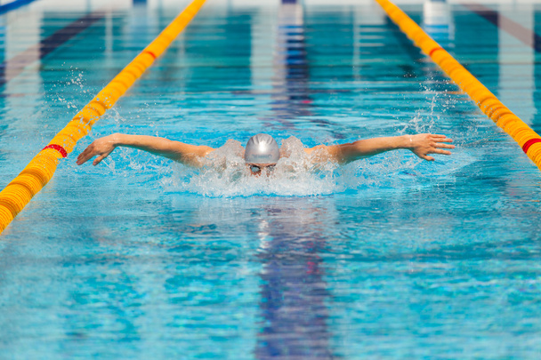 dynamic and fit swimmer in cap breathing performing the butterfly stroke - Fotó, kép