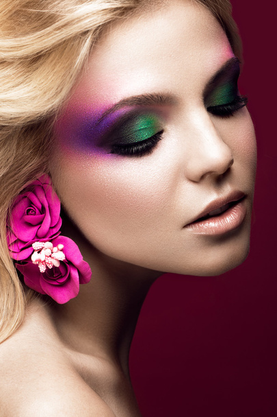 Beautiful young blonde woman with creative make-up color and flowers on the ears. Beauty face. Art makeup. - Valokuva, kuva