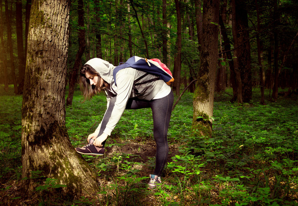 女の子が森の中の彼女のスニーカーをレースアップします。 - 写真・画像