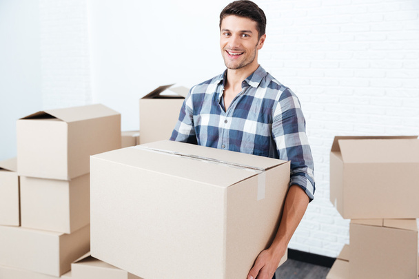Smiling happy man carrying carton boxes at new flat - Foto, immagini
