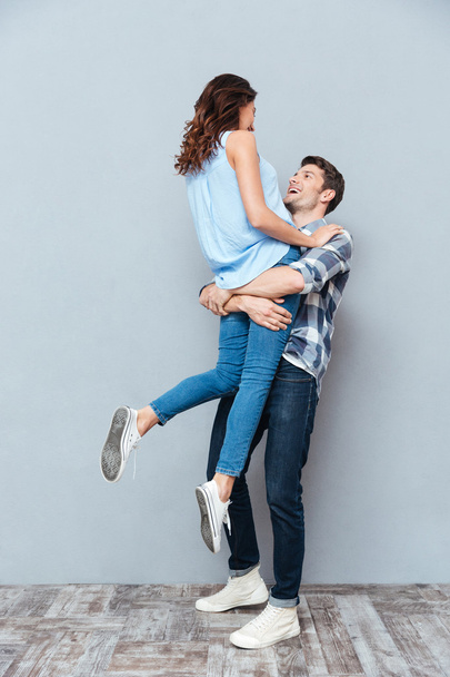 Man lifting up his girlfriend on gray background - Foto, immagini