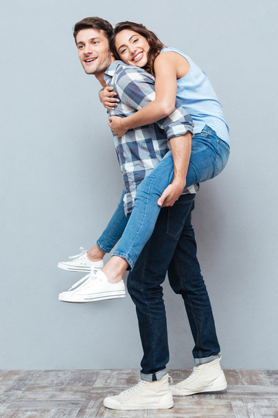 Young couple enjoying piggyback ride over gray background - Foto, afbeelding