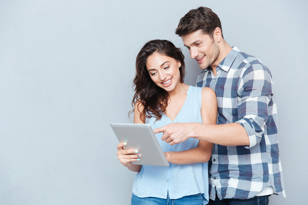 Young couple pointing at pc tablet over gray background - Foto, imagen