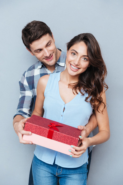 Young woman receiving gift from her boyfriend over gray background - Foto, Bild