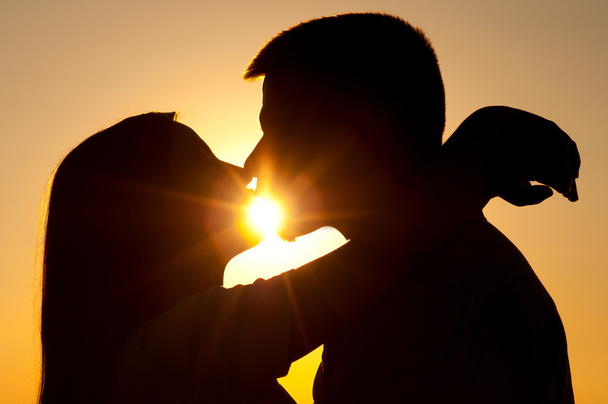 silhouetten van jonge paar zoenen op zonnige zomerdag - Foto, afbeelding