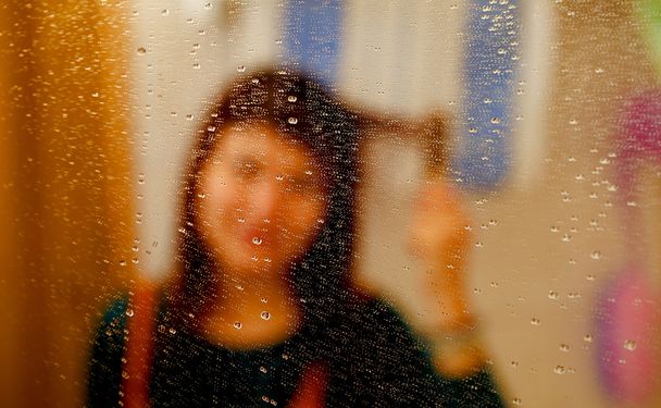 mistige reflectie van meisje in de spiegel met waterdruppeltjes. kammen van haar haren. - Foto, afbeelding