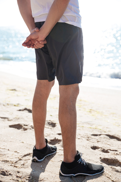 Legs of man in shorts and sneakers standing on beach - Zdjęcie, obraz